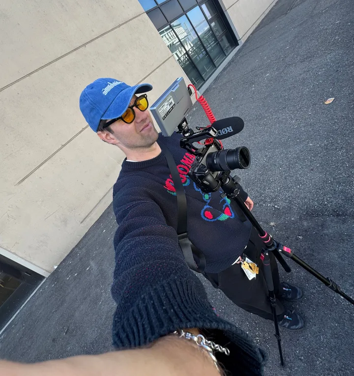 Graeme in a blue cap with a camera rig on a monopod, on a city street
